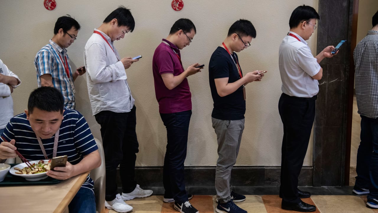 موظفون يعملون على هواتفهم الذكية أثناء انتظار دورهم لتناول الغداء في حرم دونغقوان.