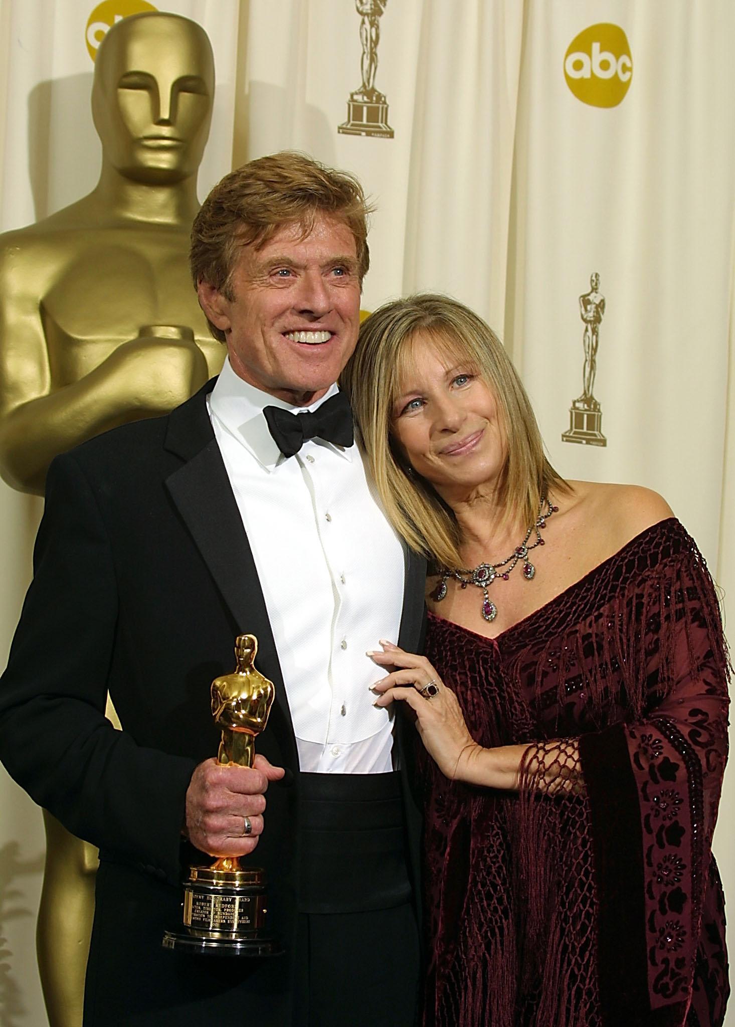 Robert Redford (L) holds his honorary Oscar presented to him by US singer and actress Barbra Streisand