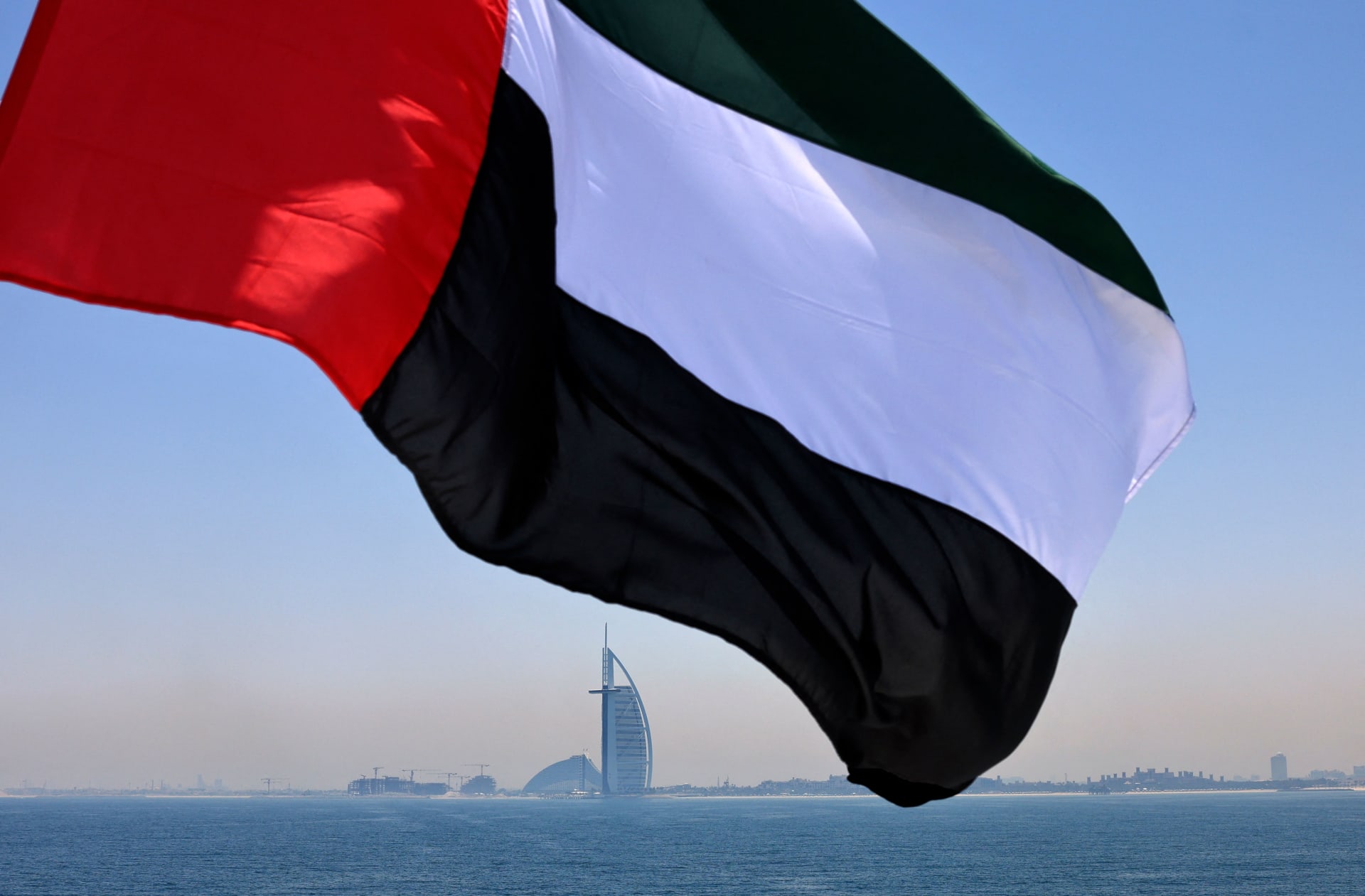علم الإمارات يرفرف فوق مرسى دبي مع فندق برج العرب في الخلفية - في 3 يونيو 2021