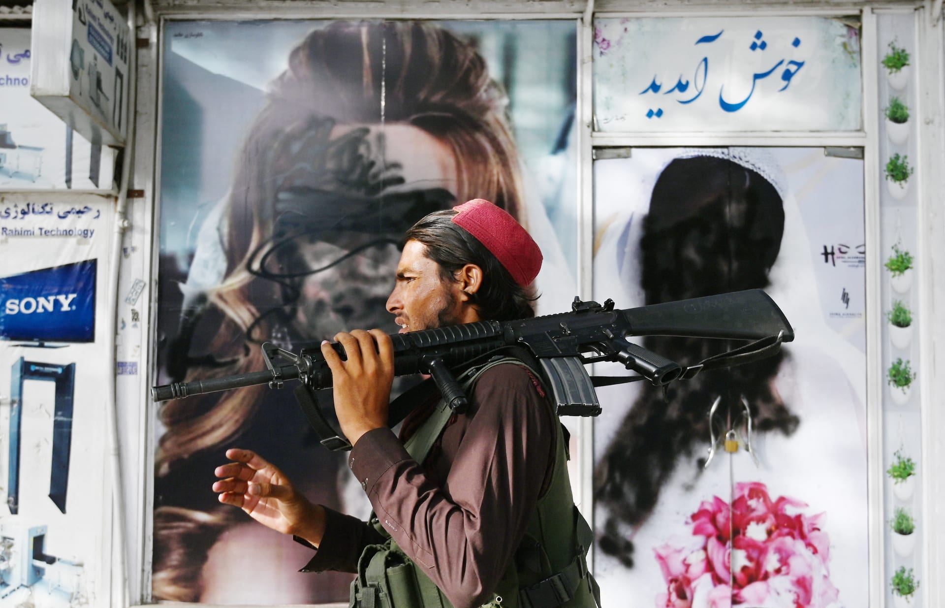 قاتل من طالبان يمشي أمام صالون تجميل مع صور لنساء مشوهات بالطلاء بالرش في شار ناو في كابول في 18 أغسطس 2021