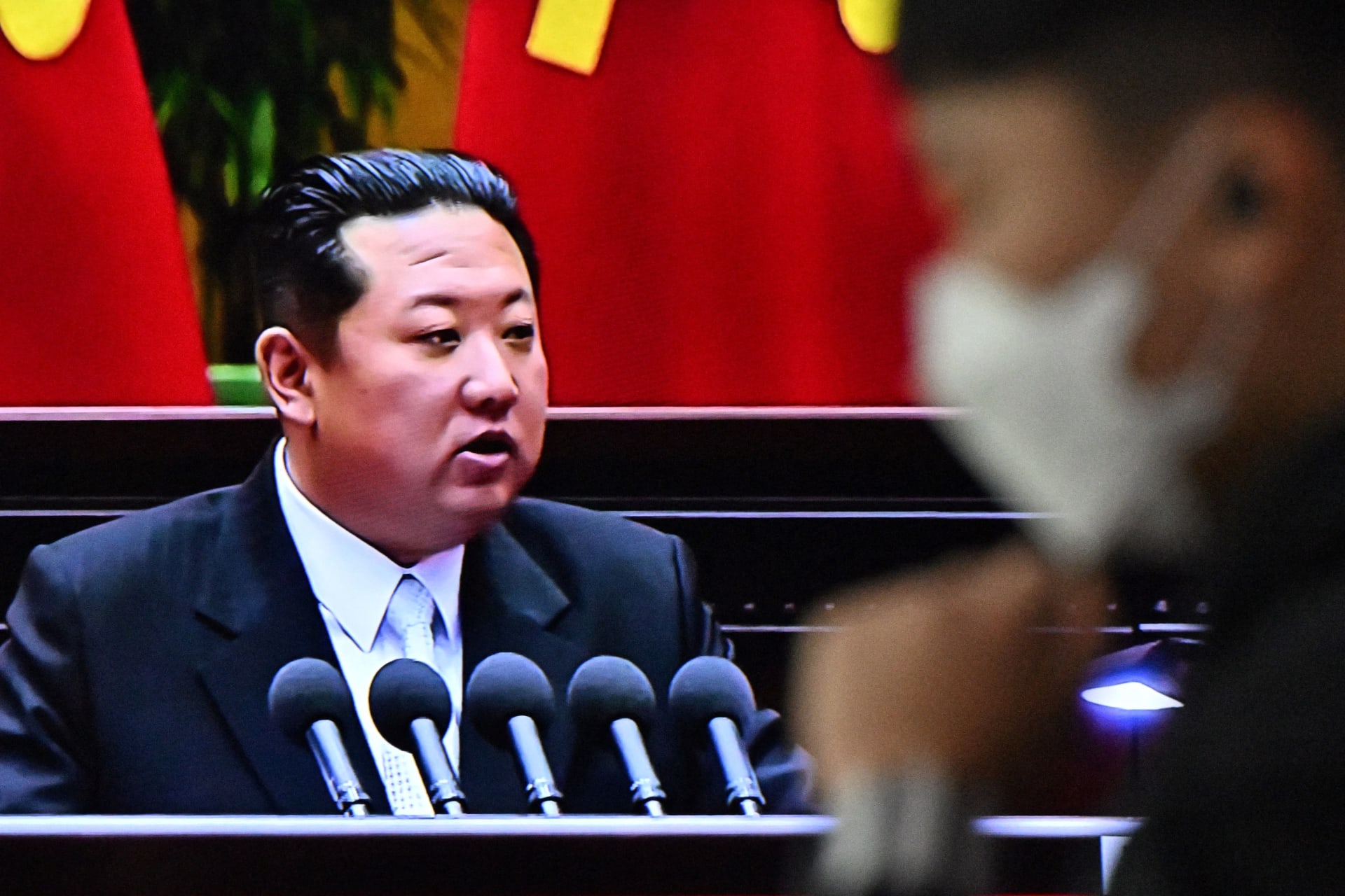 رجل يمشي أمام  تلفزيون يعرض لقطات للزعيم الكوري الشمالي كيم جونغ أون 