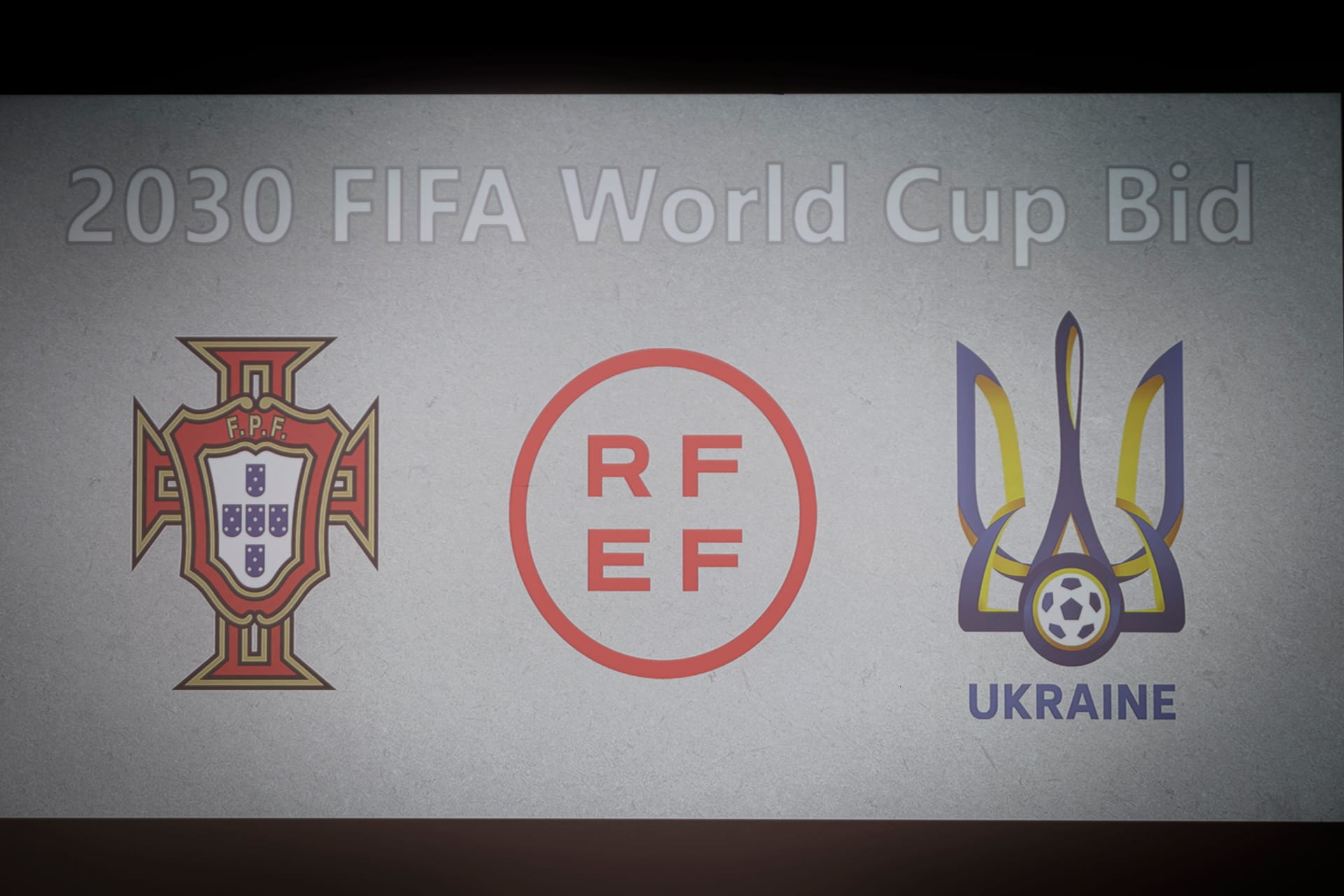 شعارات الاتحاد البرتغالي لكرة القدم (يسار) والاتحاد الإسباني لكرة القدم (وسط) والاتحاد الأوكراني لكرة القدم خلال الإعلان عن عرض  استضافة كأس العالم 2030