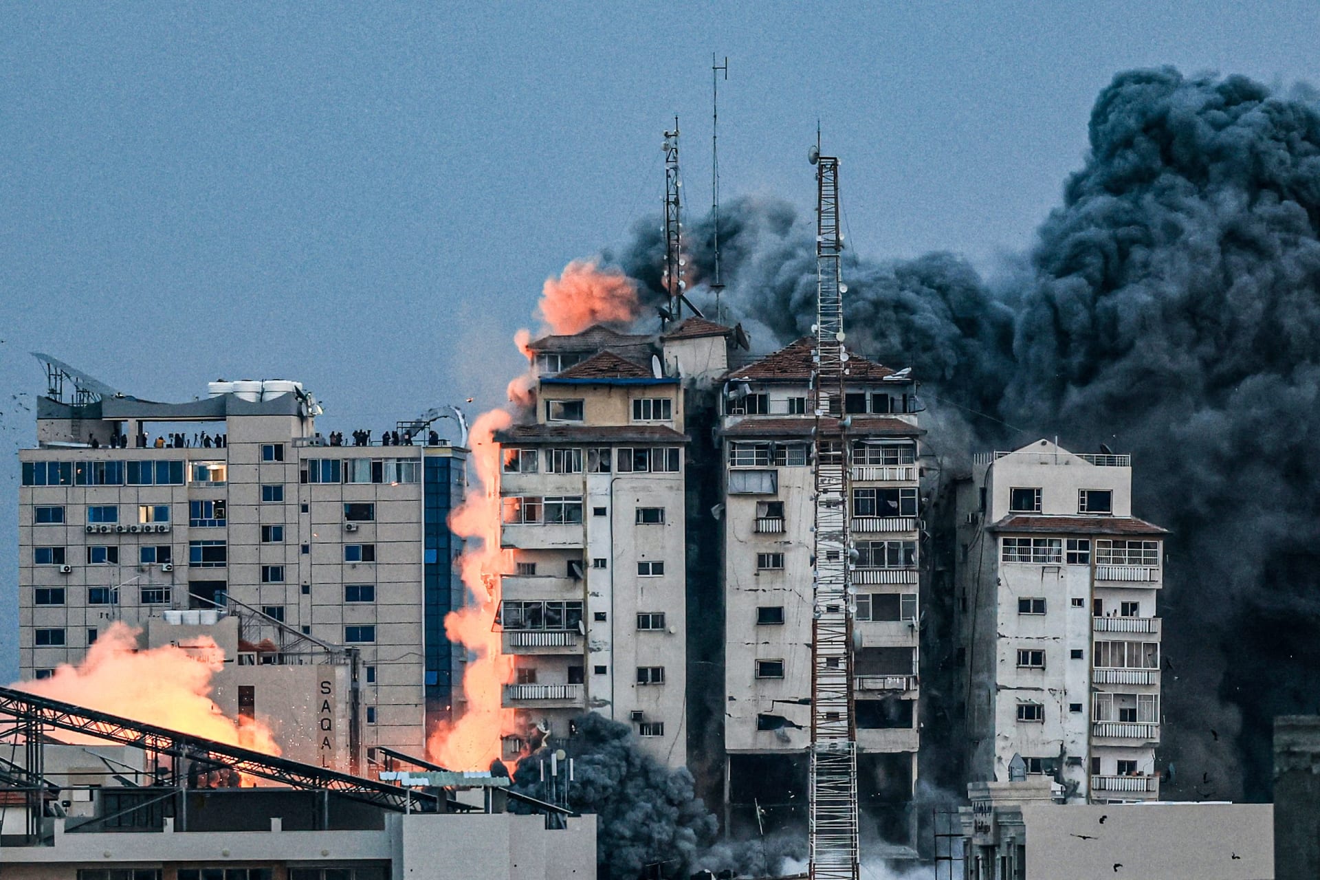 أشخاص يقفون على سطح مبنى بينما تتصاعد كرة من النار والدخان فوق برج فلسطين في مدينة غزة في 7 أكتوبر/ تشرين الأول 2023 أثناء غارة جوية إسرائيلية.