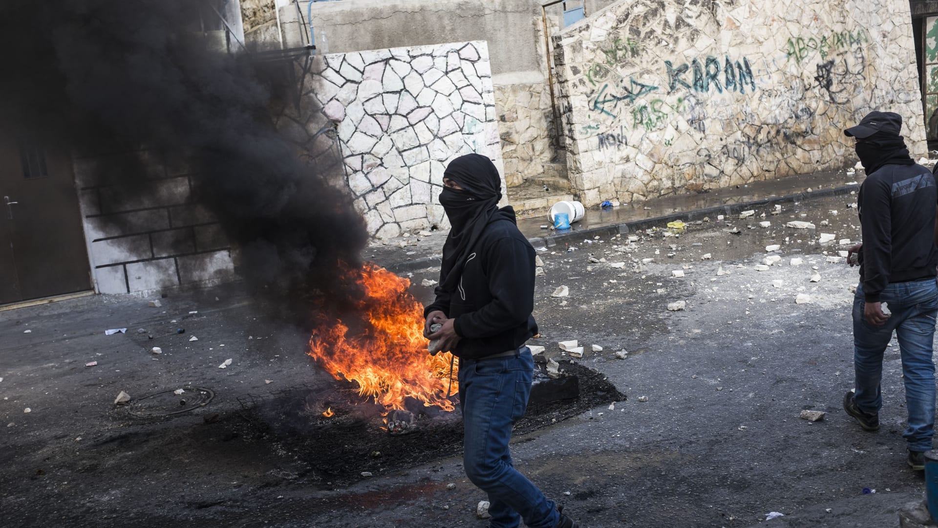 النيران تشتعل في أحد الإطارات قرب شاب فلسطيني بالقدس خلال مواجهات مع القوات الإسرائيلية.