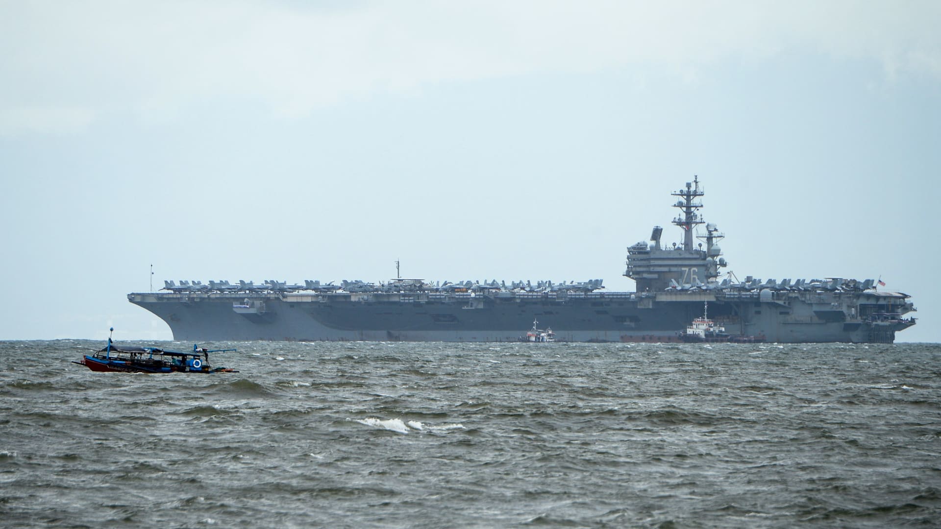 قارب صيد فلبيني (يسار) يمر بسرعة متجاوزًا يو إس إس رونالد ريغان راسيًا في خليج مانيلا في 7 أغسطس، 2019.