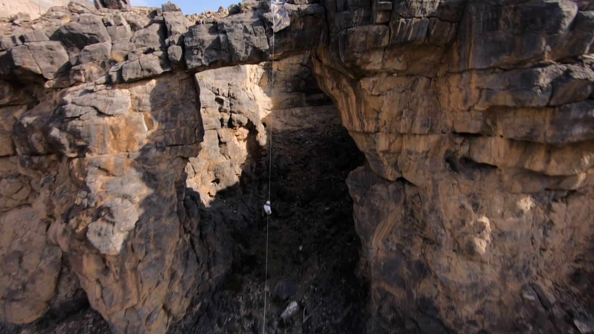 مصور يرصد مغامرًا متعلقًا على قوس صخري بسلطنة عمان ارتفاعه 35 مترًا.. شاهد