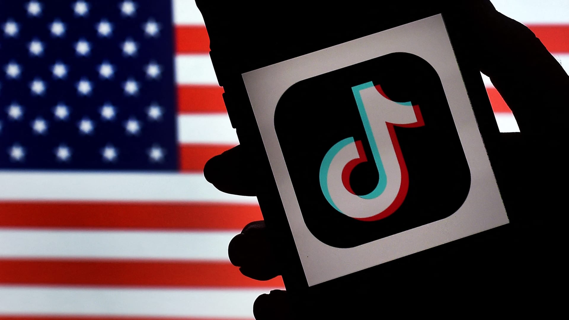 صورة تعبيرية لشغار شركة تيك توك على هاتف أمام العلم الأمريكي