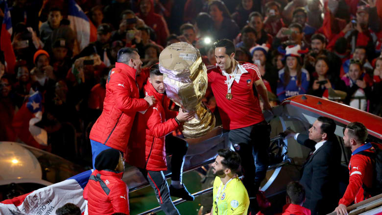 لاعبو المنتخب التشيلي يحملون الكأس على متن حافلتهم بعد فوزهم بلقب بطولة "كوبا أمريكا." لاعبو المنتخب التشيلي يحملون الكأس على متن حافلتهم بعد فوزهم بلقب بطولة "كوبا أمريكا."