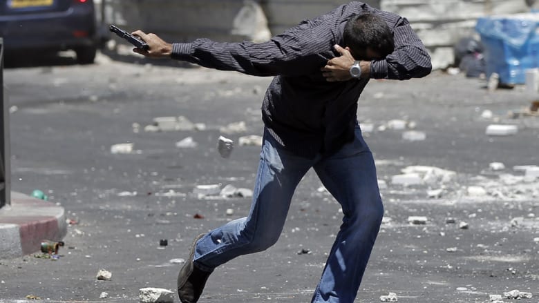 شرطي سري إسرائيلي يشهر سلاحه ويتقي حجارة المتظاهرين الفلسطينيين