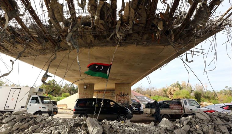 معسكر 27 ، ليبيا-- العلم الليبي يظهر تحت جسر مهدم جزئيا حيث أقامت الشرطة حاجزا على الطريق المؤدي إلى العاصمة طرابلس من جهة الغرب، حيث تتصارع مليشيات مسلحة للسيطرة على العاصمة، 9 سبتمبر 2014