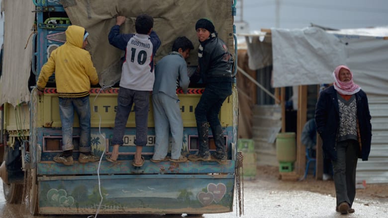 أولاد سوريون يقفون على الجزء الخلفي من شاحنة في المخيم
