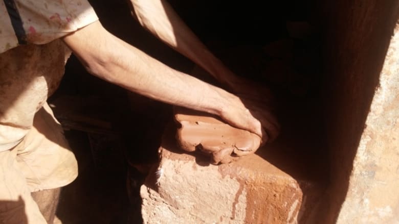 أحد الحرفيين يقوم بعجن الطين قبل صنع أشكال منه