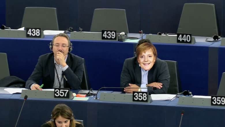 بالفيديو.. عضو بالمفوضية الأوروبية يضع قناعا لوجه ميركل خلال جلسة لمناقشة أزمة اللاجئين