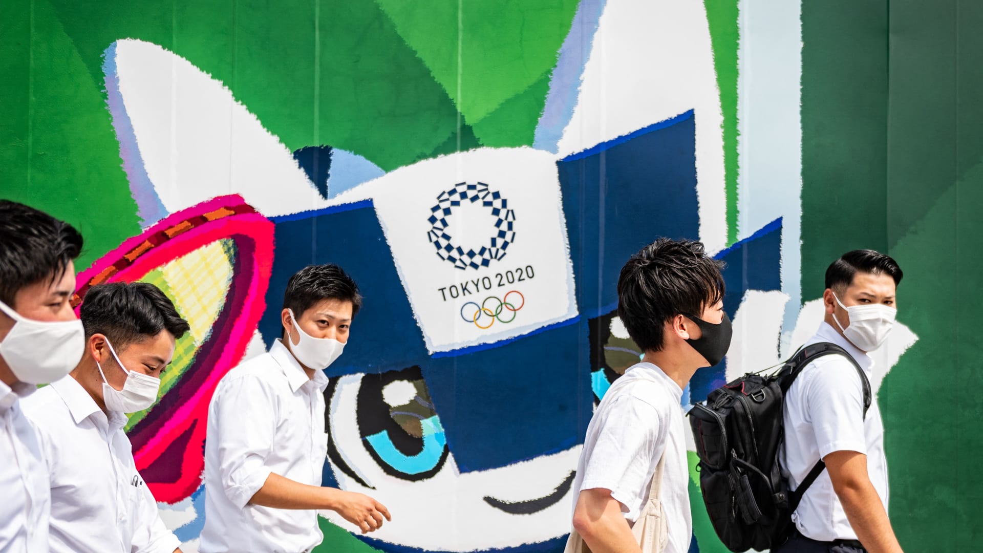 المشاة يمرون أمام لافتات أولمبية طوكيو 2020 خارج موقع بناء في طوكيو في 18 يونيو 2021
