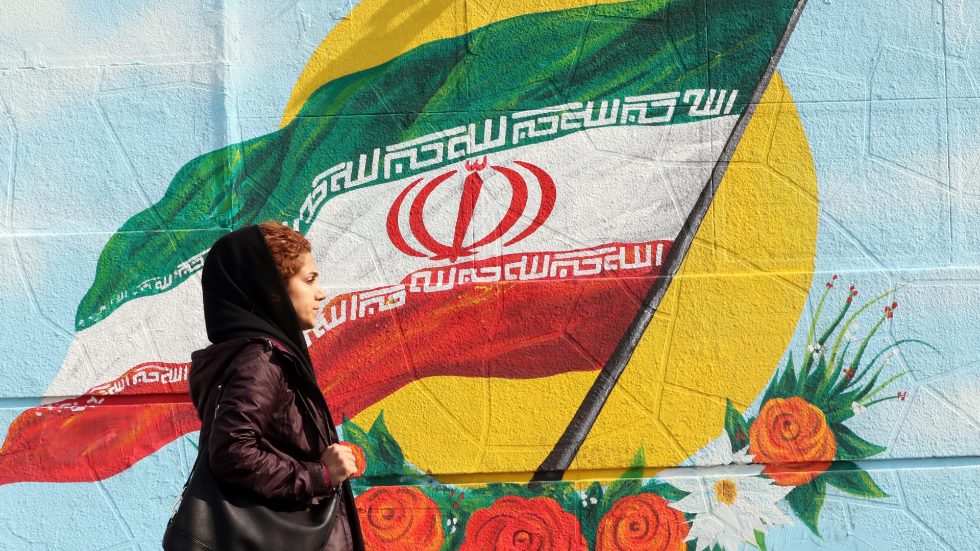 صورة ارشيفية تعبيرية لفتاة تسير أمام لوحة للعلم الإيراني 