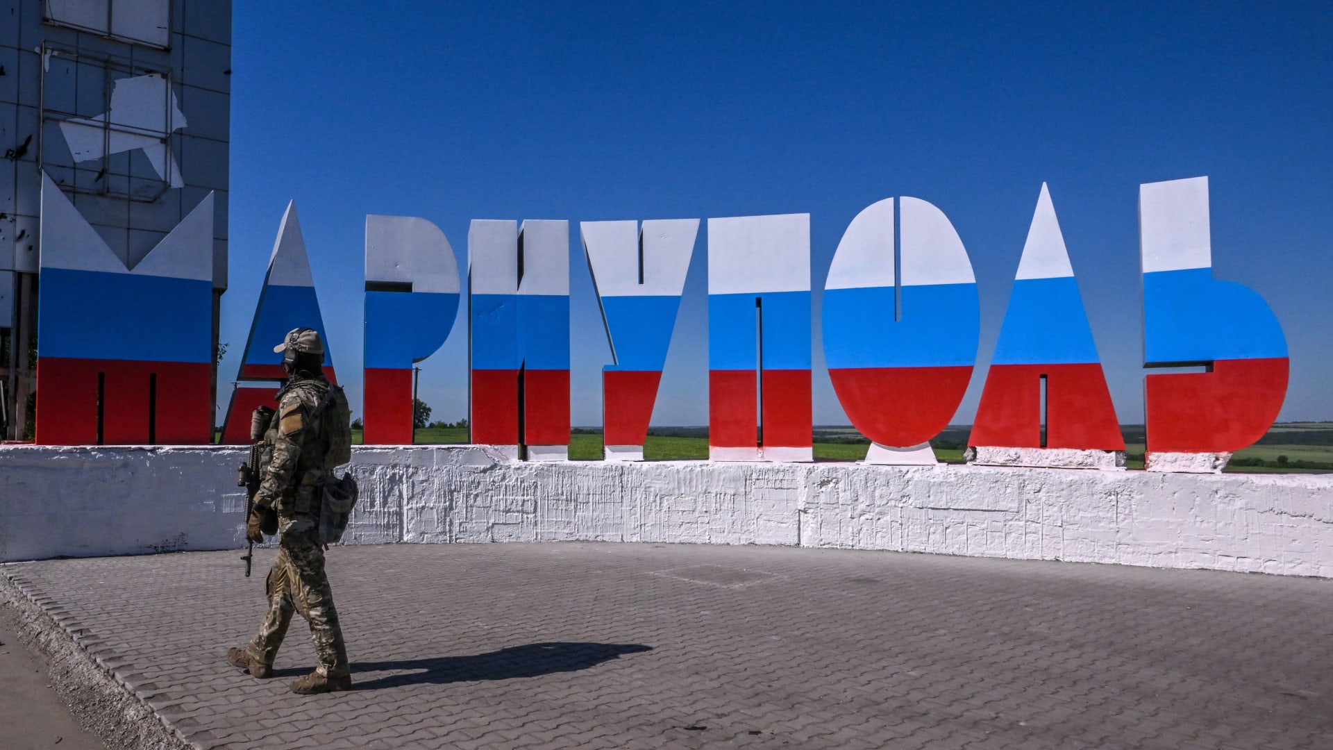 جندي روسي يسير بالقرب من لافتة ترحيب مكتوب عليها "ماريوبول" والتي تم رسمها بألوان العلم الروسي