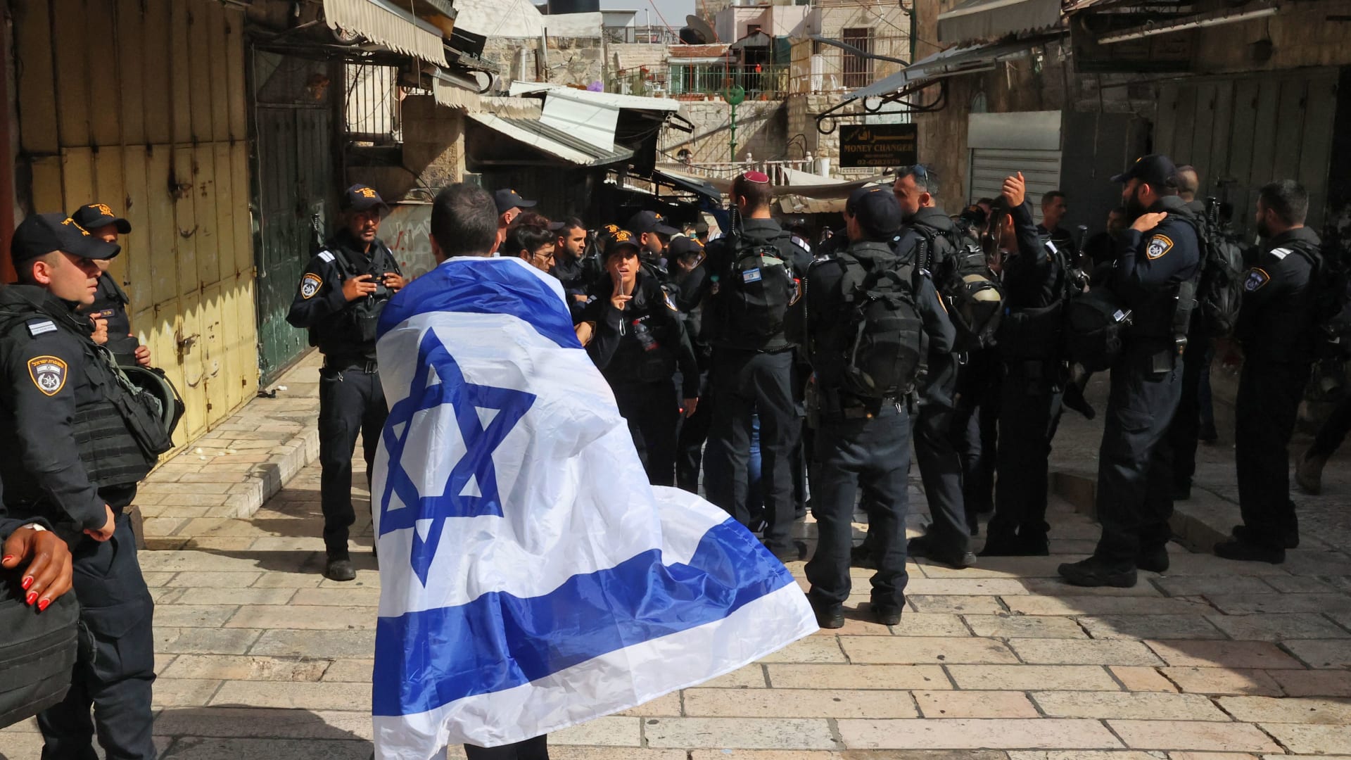 رجل ملفوف بعلم إسرائيلي يقف أمام رجال الشرطة الإسرائيلية في شارع بالبلدة القديمة بالقدس
